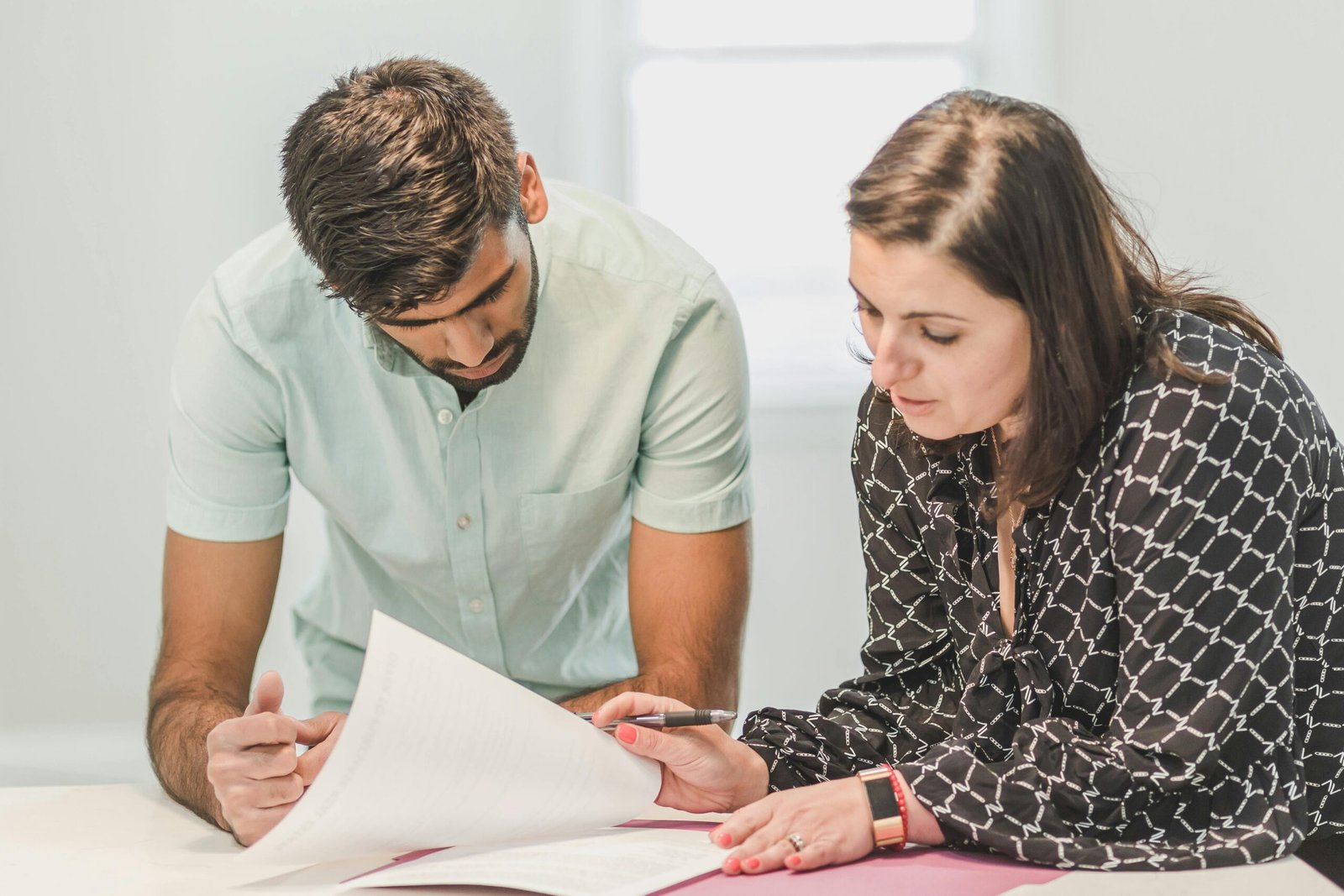 Two people leaning over a table reading a printed document together, one holding a pen